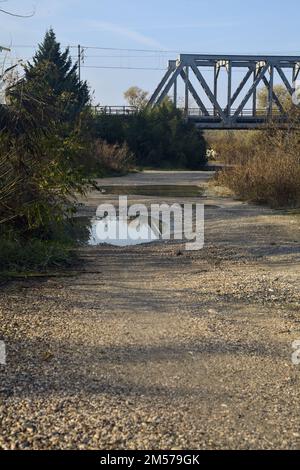 Unbefestigter Pfad mit Pfützen und einer Brücke im Hintergrund auf dem Land Stockfoto