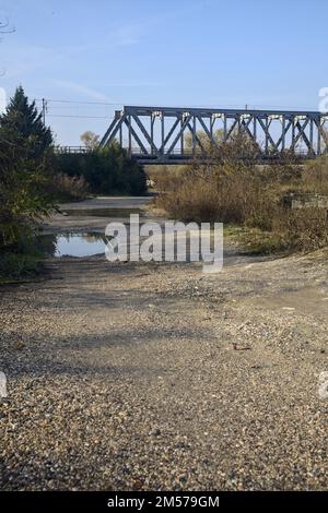 Unbefestigter Pfad mit Pfützen und einer Brücke im Hintergrund auf dem Land Stockfoto