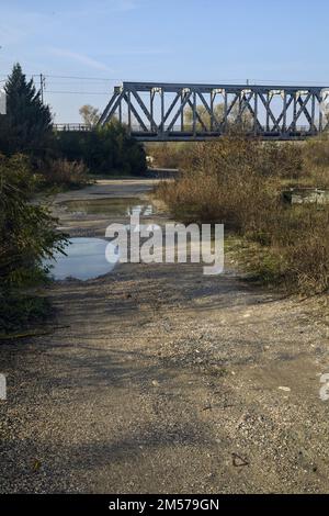 Unbefestigter Pfad mit Pfützen und einer Brücke im Hintergrund auf dem Land Stockfoto