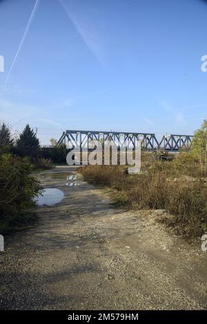 Unbefestigter Pfad mit Pfützen und einer Brücke im Hintergrund auf dem Land Stockfoto
