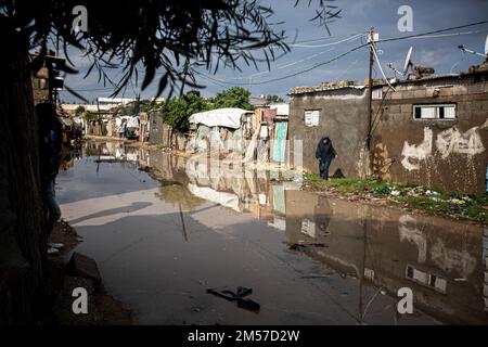 Gaza, Palästina. 26. Dezember 2022. Eine palästinensische Frau läuft auf einer mit Regenwasser überfluteten Straße in einem armen Viertel am Rande des Flüchtlingslagers Khan Yunis im südlichen Gazastreifen. Kredit: SOPA Images Limited/Alamy Live News Stockfoto