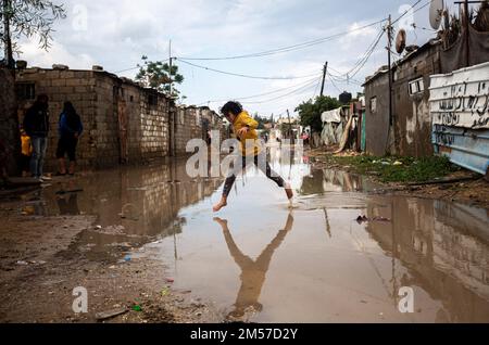 Gaza, Palästina. 26. Dezember 2022. Ein palästinensisches Mädchen springt auf eine wasserdurchlässige Straße in Khan Yunis, im südlichen Gazastreifen. Kredit: SOPA Images Limited/Alamy Live News Stockfoto