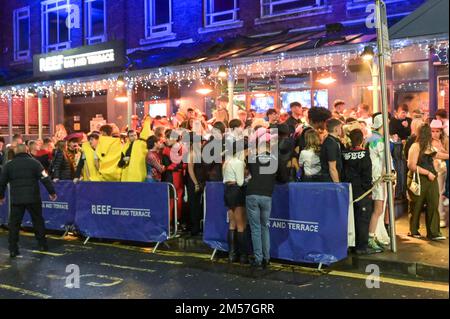 King Street, Wigan, 27. 2022. Dezember. - Reveller stolperten nach Hause und ruhten sich gegen Gebäude und auf Gehwegen aus, nach einem schönen Abend am Boxing Day, der alljährlichen Fancy Dress Night in Wigan. Ein paar Verkehrskegel stellten sicher, dass es einer Frau gut ging, als sie auf einem Bordstein saß. Ein Mann in einem Frauenkleid, Freddie Mercury-Stil, wurde angeschrien und von einer anderen Frau außerhalb von Popworld weggestoßen. Einige nahmen sich ein Essen mit, um die Nacht davor zu genießen, als sie auf Taxis warteten. Stockfoto