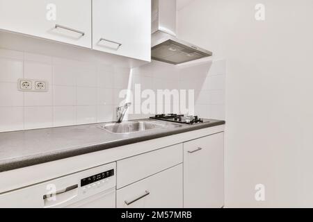 Eine Küche mit weißen Schränken und schwarzen Ablageflächen auf den Ablagen vor dem Geschirrspüler gibt es ein Gerät Stockfoto