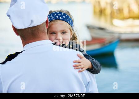 Daddys kommen nach Hause. Rückblick auf einen Vater in Navy-Uniform, der sein glückliches kleines Mädchen umarmt. Stockfoto