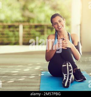 Ich fühle mich besser als Sport. Porträt einer sportlichen jungen Frau, die auf ihrer Yoga-Matte sitzt. Stockfoto