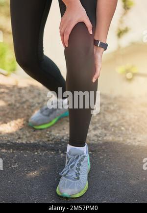 Spürt die Auswirkungen eines anstrengenden Laufs. Eine nicht wiedererkennbare junge Frau, die ihr Knie während ihres Morgenlaufs vor Schmerzen hielt. Stockfoto