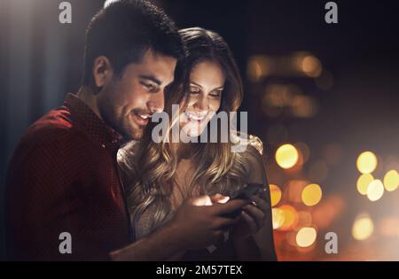 Wir tauschen Nummern aus. Ein junges Paar, das nachts seine Smartphones zusammen benutzt. Stockfoto