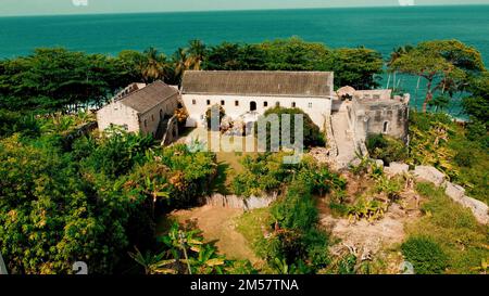 Ein altes Gebäude, umgeben von tropischen Bäumen an einer Küste an einem sonnigen Tag Stockfoto