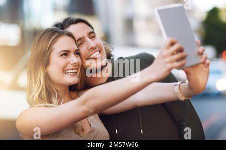 Ich habe die perfekte Übereinstimmung gefunden. Porträt eines glücklichen jungen Paares, das ein Selfie auf seinem digitalen Tablet macht. Stockfoto