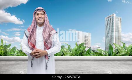 Ein arabischer Mann, der Keffiyeh trägt und agal in der Stadt steht, mit blauem Hintergrund Stockfoto