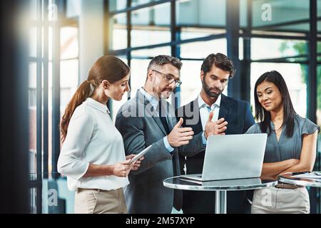 Taten folgen lassen. Eine Gruppe von Kollegen, die gemeinsam ein Notebook in einem modernen Büro verwenden. Stockfoto