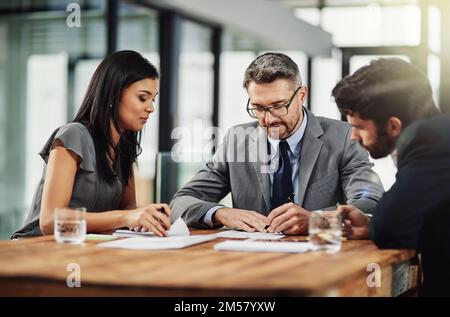 Um den Sitzungstisch. Drei Kollegen, die im Büro um ein Tablet sitzen. Stockfoto