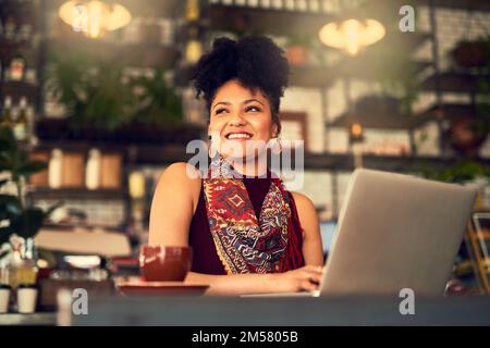 Zeit, sich anzumelden und zu entspannen. Eine attraktive junge Frau, die in einem Café an ihrem Laptop arbeitet. Stockfoto