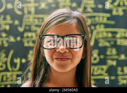 Sie ist neugierig und neugierig. Porträt eines kleinen Mädchens, das gegen eine Tafel posiert, mit Mathematikgleichungen. Stockfoto