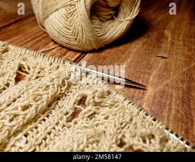 Durchbrochene Tischdecke beim Stricken. Stricknadeln, Schlaufen auf Stricknadeln, Strickstoff, Fadenknäuel, grobe Baumwolle und Leinen Stockfoto