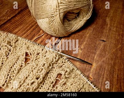 Durchbrochene Tischdecke beim Stricken. Stricknadeln, Schlaufen auf Stricknadeln, Strickstoff, Fadenknäuel, grobe Baumwolle und Leinen Stockfoto