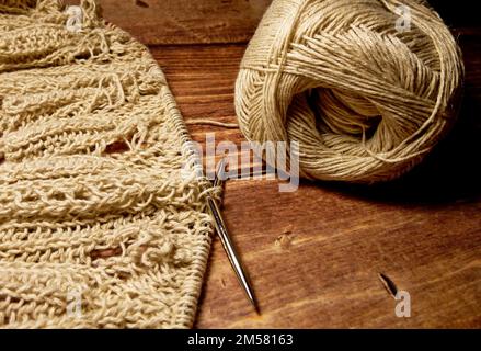 Durchbrochene Tischdecke beim Stricken. Stricknadeln, Schlaufen auf Stricknadeln, Strickstoff, Fadenknäuel, grobe Baumwolle und Leinen Stockfoto