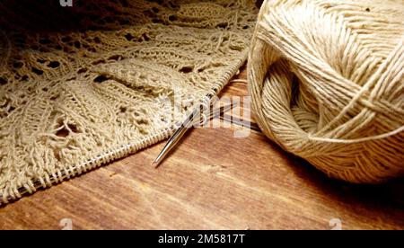 Durchbrochene Tischdecke beim Stricken. Stricknadeln, Schlaufen auf Stricknadeln, Strickstoff, Fadenknäuel, grobe Baumwolle und Leinen Stockfoto