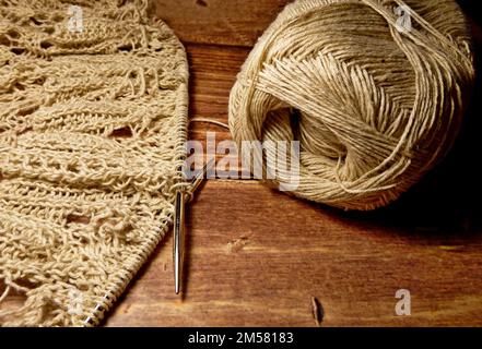 Durchbrochene Tischdecke beim Stricken. Stricknadeln, Schlaufen auf Stricknadeln, Strickstoff, Fadenknäuel, grobe Baumwolle und Leinen Stockfoto
