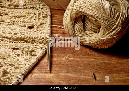 Durchbrochene Tischdecke beim Stricken. Stricknadeln, Schlaufen auf Stricknadeln, Strickstoff, Fadenknäuel, grobe Baumwolle und Leinen Stockfoto