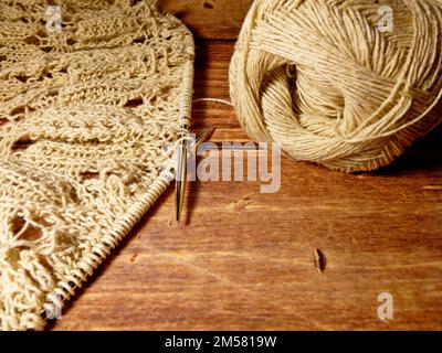 Durchbrochene Tischdecke beim Stricken. Stricknadeln, Schlaufen auf Stricknadeln, Strickstoff, Fadenknäuel, grobe Baumwolle und Leinen Stockfoto
