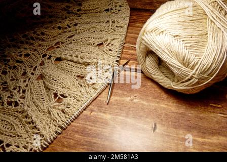 Durchbrochene Tischdecke beim Stricken. Stricknadeln, Schlaufen auf Stricknadeln, Strickstoff, Fadenknäuel, grobe Baumwolle und Leinen Stockfoto