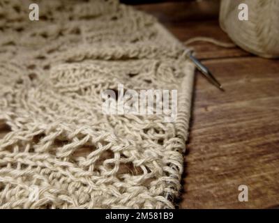 Durchbrochene Tischdecke beim Stricken. Stricknadeln, Schlaufen auf Stricknadeln, Strickstoff, Fadenknäuel, grobe Baumwolle und Leinen Stockfoto