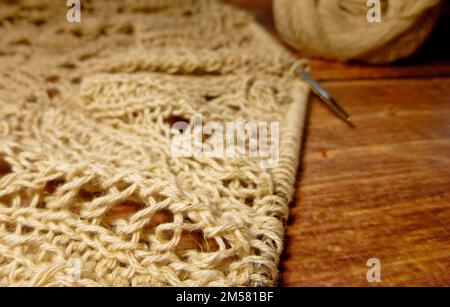 Durchbrochene Tischdecke beim Stricken. Stricknadeln, Schlaufen auf Stricknadeln, Strickstoff, Fadenknäuel, grobe Baumwolle und Leinen Stockfoto