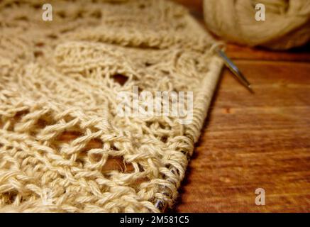 Durchbrochene Tischdecke beim Stricken. Stricknadeln, Schlaufen auf Stricknadeln, Strickstoff, Fadenknäuel, grobe Baumwolle und Leinen Stockfoto