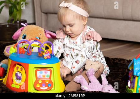 Ein glückliches eineinhalb Jahre altes Mädchen spielt mit Spielzeug, das auf dem Boden liegt. Stockfoto
