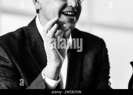 Schließen. Lächelnder Geschäftsmann, der am Tisch sitzt und die OK-Geste zeigt. Stockfoto