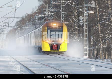 Der gelbe Hochgeschwindigkeitszug fährt mit hoher Geschwindigkeit und hinterlässt im Winter Staub aus Schnee und Schneesturm in der verschneiten Landschaft Stockfoto