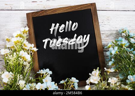 „Hello Tuesday“-Textnachricht mit Blumendekoration auf Holzhintergrund Stockfoto