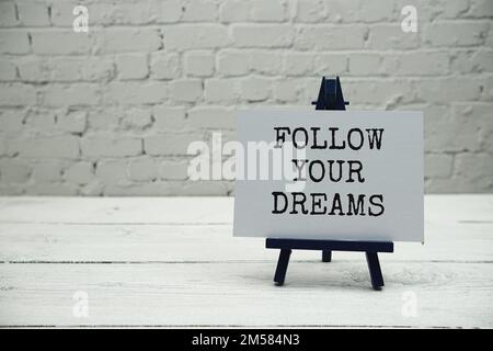Folgen Sie Ihrem Traumtext auf weißen Backsteinwänden und Holzhintergrund Stockfoto