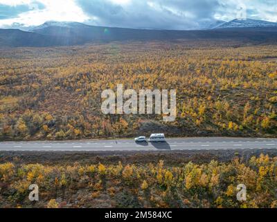 Luftaufnahmen von Car Camping Caravan, die auf der Straße am See tief im schwedischen Lappland unterwegs sind. Sonniger Tag und Herbstfarben im Abisko-Nationalpark Schweden Stockfoto