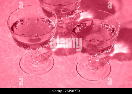 Drei Kristallgläser Sekt oder Champagner. Getöntes Bild in trendy magentafarbener Farbe des Jahres 2023. Minimale kreative Komposition mit Kopierraum. Stockfoto