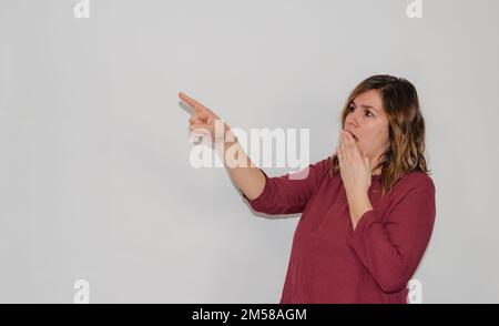 Eine Frau auf weißem Hintergrund, die überraschend auf den Kopierraum zeigt Stockfoto
