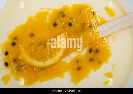 Orangen- und Passionsfrucht-Eis am Stiel mit einer Scheibe Orangen, geschmolzen auf einem Gericht mit Zeitfenster Stockfoto