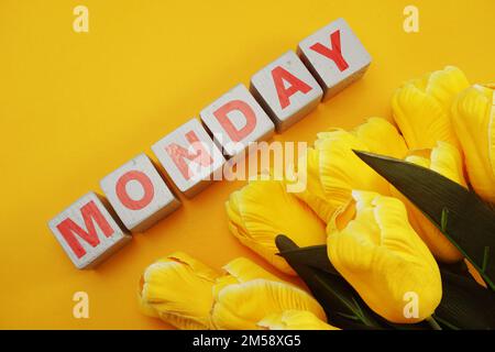 Montags ein hölzernes Alphabet mit Tulpenblüten auf gelbem Hintergrund Stockfoto