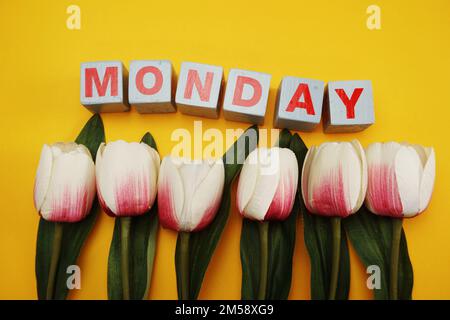 Montags ein hölzernes Alphabet mit Tulpenblüten auf gelbem Hintergrund Stockfoto