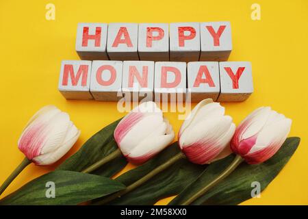 Happy Monday – ein hölzernes Alphabet mit Tulpenblüten auf gelbem Hintergrund Stockfoto