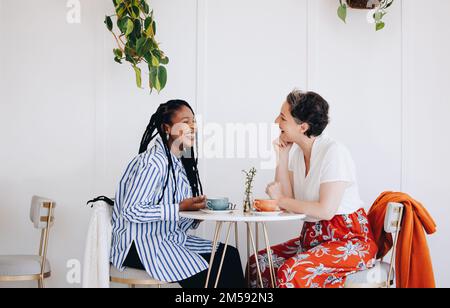 Zwei glückliche Geschäftsfrauen, die sich während einer Kaffeepause in einem Café unterhalten und lachen. Fröhliche Geschäftskollegen, die einen freundlichen Konver genießen Stockfoto
