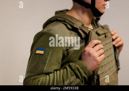 Streitkräfte der Ukraine. Ukrainischer Soldat steht und hält sich an Körperpanzerung. Ukrainische Armee. Ukrainische Flagge auf Militäruniform. Stockfoto