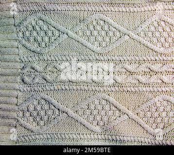 Die Konsistenz eines großen Strickpulvers oder Schals. Gestrickter Hintergrund mit Reliefmuster. Wollhandstricken oder maschinelles Stricken. Stoffhintergrund. Stockfoto