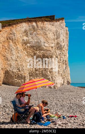 England, East Sussex, Eastbourne, The Seven Sisters Cliffs, The Birling Gap, Family with Colourful Parasol Relaxing on Beach *** Lokale Beschriftung *** Großbritannien Stockfoto