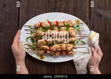Gegrilltes Gemüse und Hähnchenspieße mit Paprika, Zucchini, Zwiebeln und Pilzen auf einem Holztisch in weiblichen Händen, Draufsicht. Fleisch und Gemüse Stockfoto