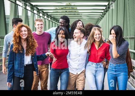 Lächelnde junge Menschen, eine große Gruppe von Frauen und Männern der Generation Z, junge Studenten, die spazieren gehen und Spaß im Freien in einem Stadtpark haben Stockfoto
