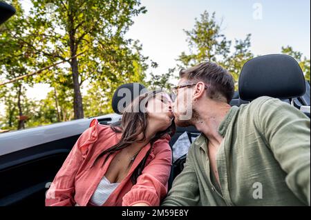 Sei mein Valentinstag, junges Paar, das ein Liebeskuss-Porträt, Roadtrip für die Flitterwochen, Grillfreund und Freunde, die sich in einem Cabrio küssen Stockfoto