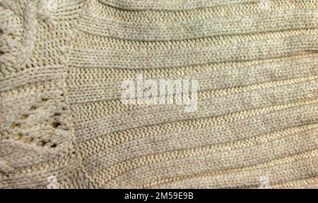 Die Konsistenz eines großen Strickpulvers oder Schals. Gestrickter Hintergrund mit Reliefmuster. Wollhandstricken oder maschinelles Stricken. Stoffhintergrund. Stockfoto